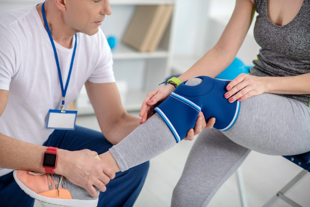 Male physiotherapist examining knee of female patient sitting on couch