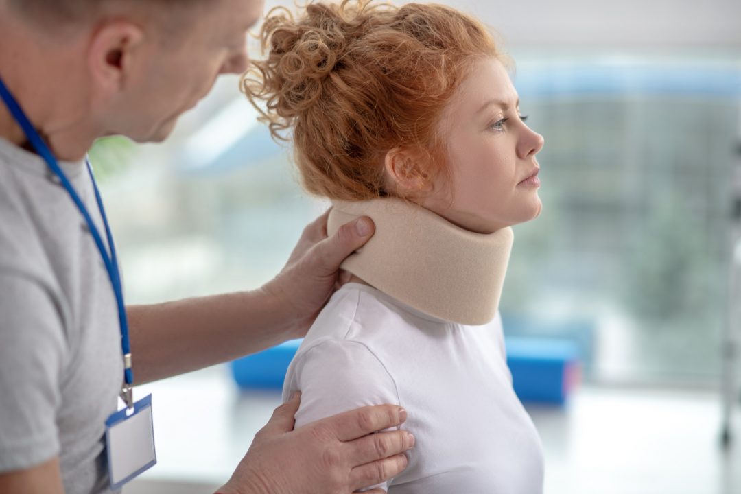 Male physiotherapist examining neck fixator of female patient